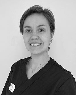 Svartvit porträttbild av en leende person med kort, sidokammat hår, iförd mörka arbetskläder och namnbricka, mot en ljus bakgrund.