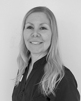 Svartvit porträttbild av en leende kvinna med långt ljust hår som faller över axlarna, iförd en mörk topp, mot en ljus bakgrund.