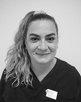 Porträtt av en leende kvinnlig tandläkare med uppsatt blont hår och svart klinikklädsel, som ger ett professionellt intryck.
