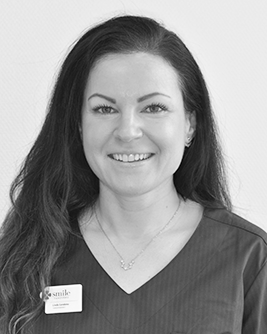 Porträtt som föreställer en kvinnlig tandhygienist med långt mörkt hår och ett varmt leende som tittar rakt in i kameran.