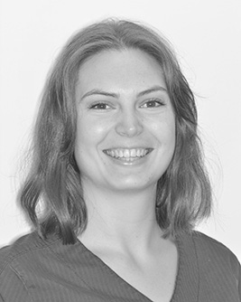 Leende tandläkare med axellångt hår, fotograferad i svartvitt mot en ljus bakgrund.
