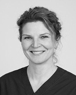 Leende tandläkare med uppsatt hår, fotograferad i svartvitt mot en ljus bakgrund.