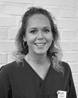 Porträtt av en leende tandhygienist med ljust hår. Bilden är i svartvitt och tagen mot en ljus bakgrund.