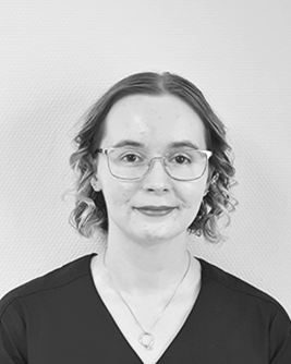Ung kvinna med kort, blont hår som står i arbetskläder framför en vit vägg.