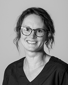 Porträtt av en leende tandläkare med glasögon och uppsatt hår, fotograferad mot en neutral bakgrund.