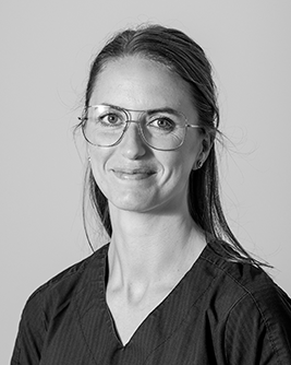 Porträtt av en tandsköterska med långt hår och glasögon, fotograferad mot en neutral bakgrund.