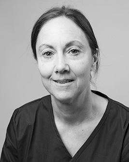 Svartvit porträttbild av en leende person med kort, sidokammat hår, iförd mörka arbetskläder och namnbricka, mot en ljus bakgrund.