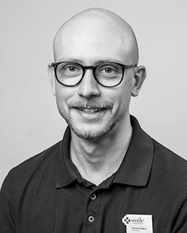 Porträtt av en manlig tandläkare med ett professionellt och vänligt uttryck.