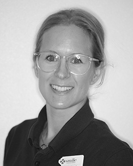 Leende kvinnlig tandshygienist med glasögon och ljust uppsatt hår.