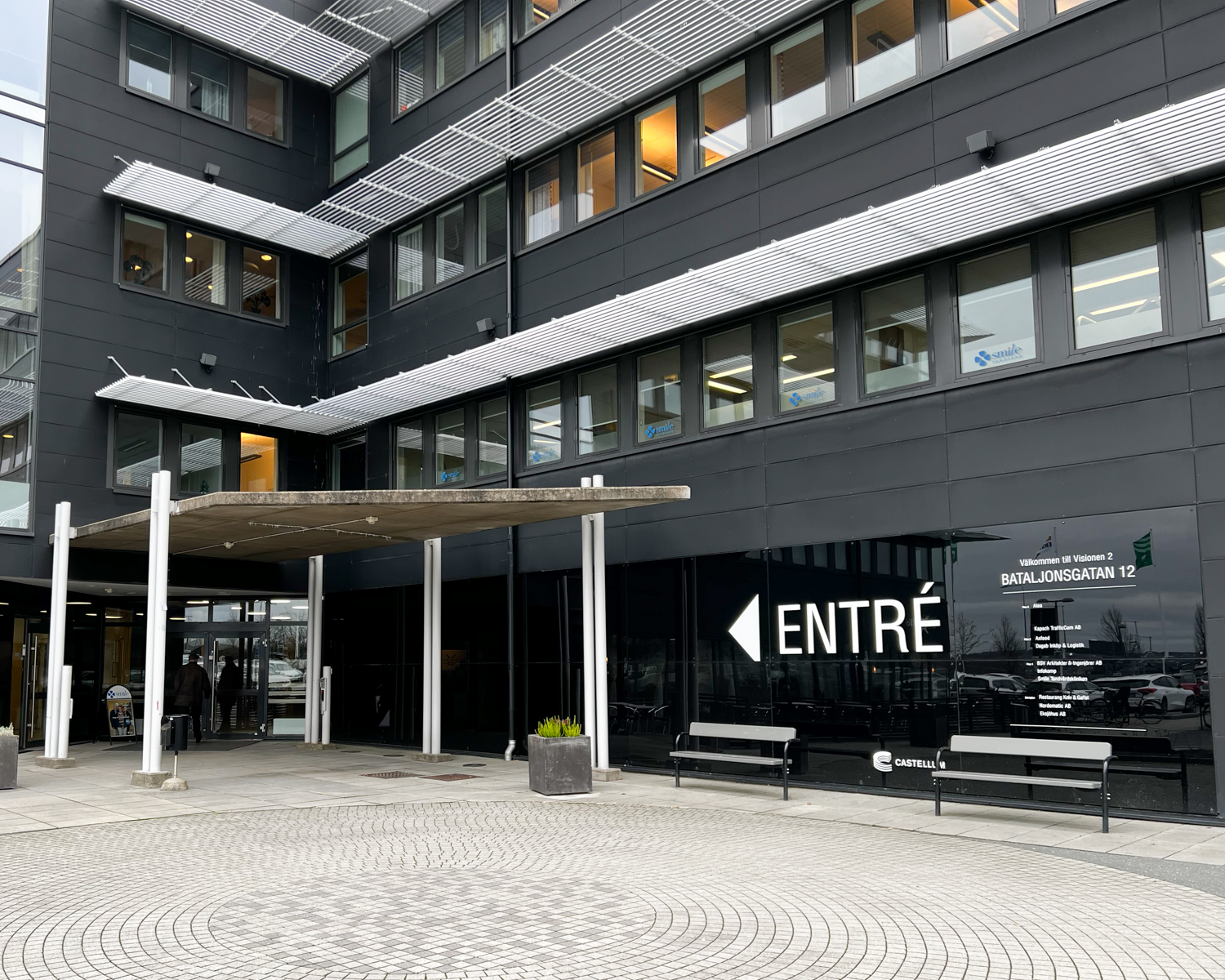 Bild av entrén till Smile Tandvård i Jönköping A6, en modern byggnad med mörka fasader och tydlig skyltning, med bänkar utanför.