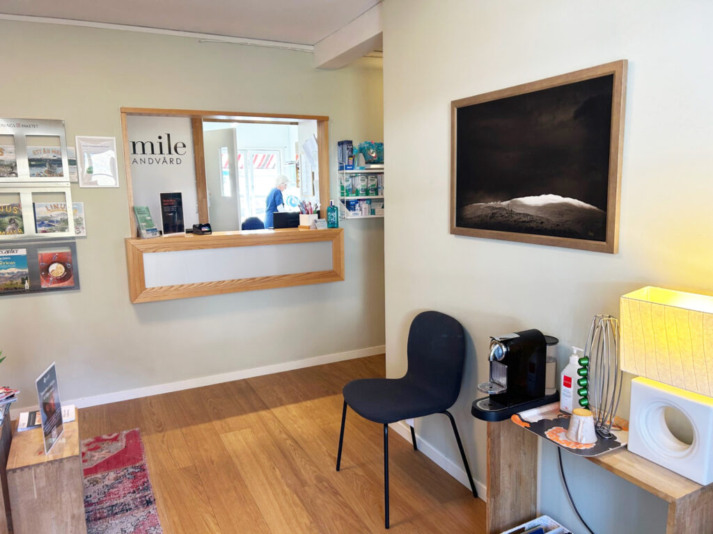 Ett ljust och modernt väntrum hos en tandläkare i Åre med stilren inredning och lugn atmosfär. Rummet har ljusa väggar, trägolv och bekväma stolar där patienter kan koppla av inför sin behandling. På väggarna syns konst och informationsmaterial om tandvård. Denna tandklinik i Åre erbjuder en trygg och professionell miljö för både vuxna och barn som söker högkvalitativ tandvård i Åre.