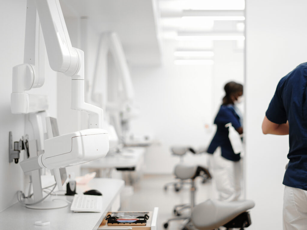 Interiör av behandlingsrum på Smile-kliniken i Boden, där tandvårdspersonal i blå arbetskläder förbereder utrustning. Bilden visar moderna tandvårdsinstrument och stolar längs väggarna. Rummet är ljust och sterilt, med fokus på effektivitet och hygien.