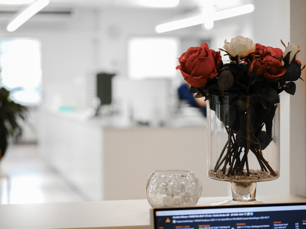 Interiörbild från Smile-kliniken i Boden, med en bukett konstgjorda blommor i förgrunden. I bakgrunden syns en ljus och modern klinikmiljö med tandvårdsutrustning och ett behandlingsrum, delvis suddigt för att fokusera på blommorna.