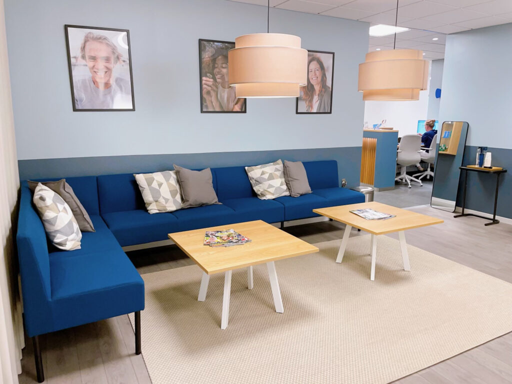 Väntrum på Smile Tandvård Hagastaden med en blå soffa, träbord och modern belysning i en ljus och inbjudande miljö.