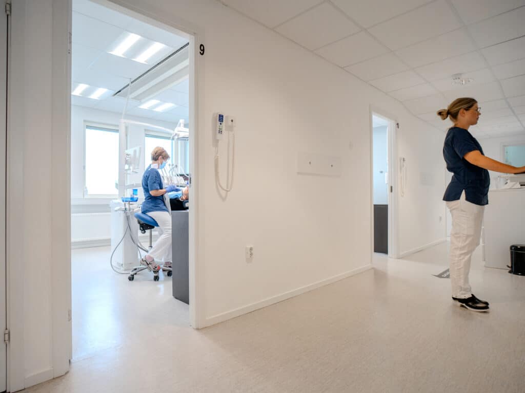 Tandläkare och personal på Smile Tandvård i arbete, med en ljus korridor och behandlingsrum i bakgrunden.