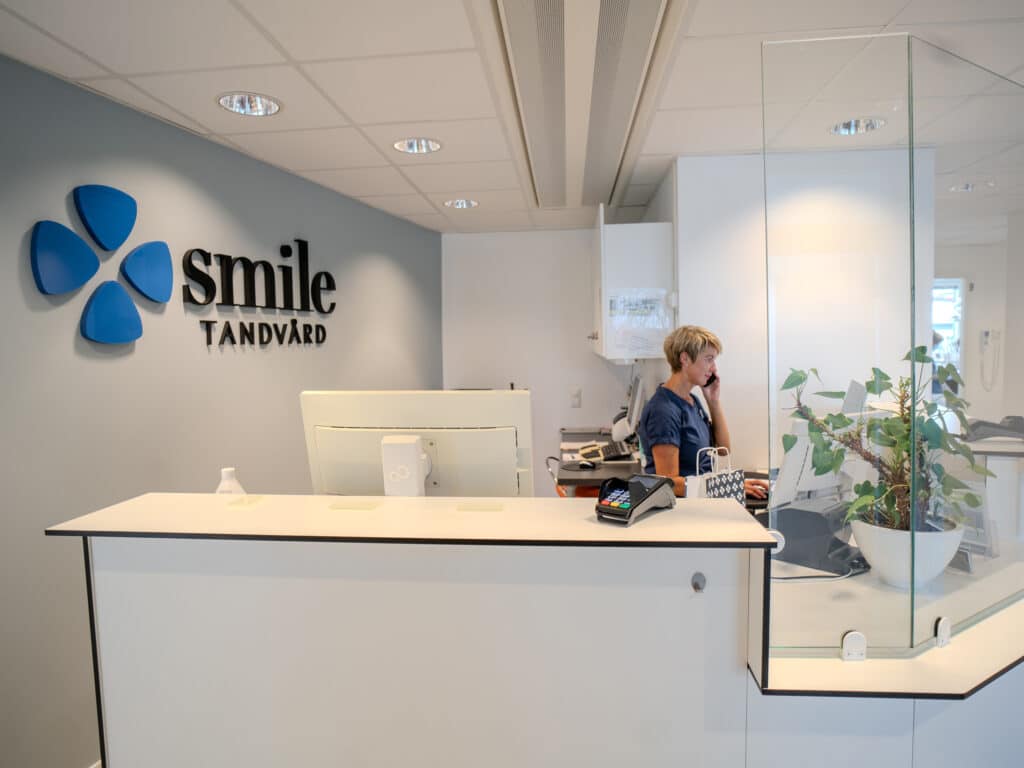 Reception på Smile Tandvård Jönköping City med en receptionist vid disken och klinikens logotyp på väggen.
