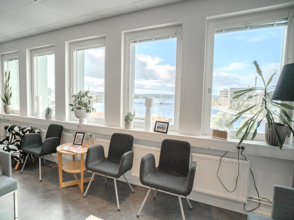 Väntrum på Smile Tandvård med svarta stolar och stora fönster som erbjuder en ljus och rymlig atmosfär med utsikt över staden.