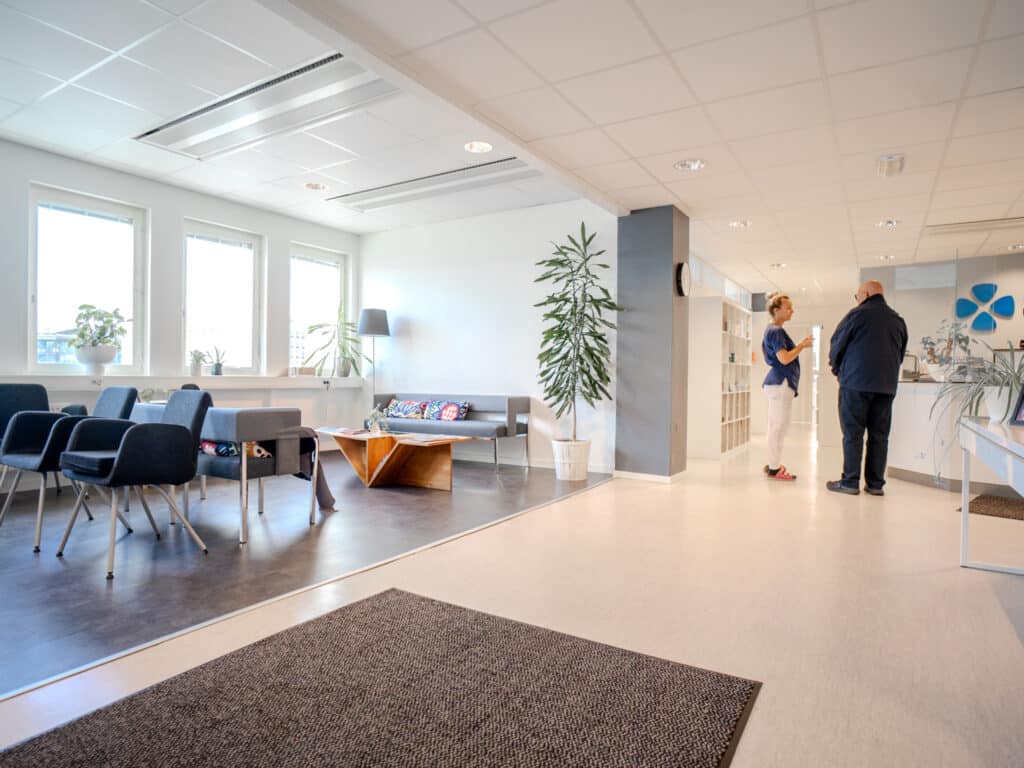 Väntrum på Smile Tandvård Jönköping City med svarta stolar, vita väggar och personal som pratar med patient vid receptionen.