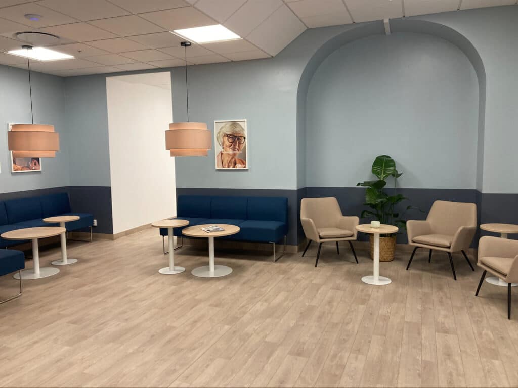 Modernt väntrum på Smile Karlskrona med bekväma sittplatser, soffor och stolar i ljusa färger, träbord och växter i en lugnande miljö med dämpad belysning.