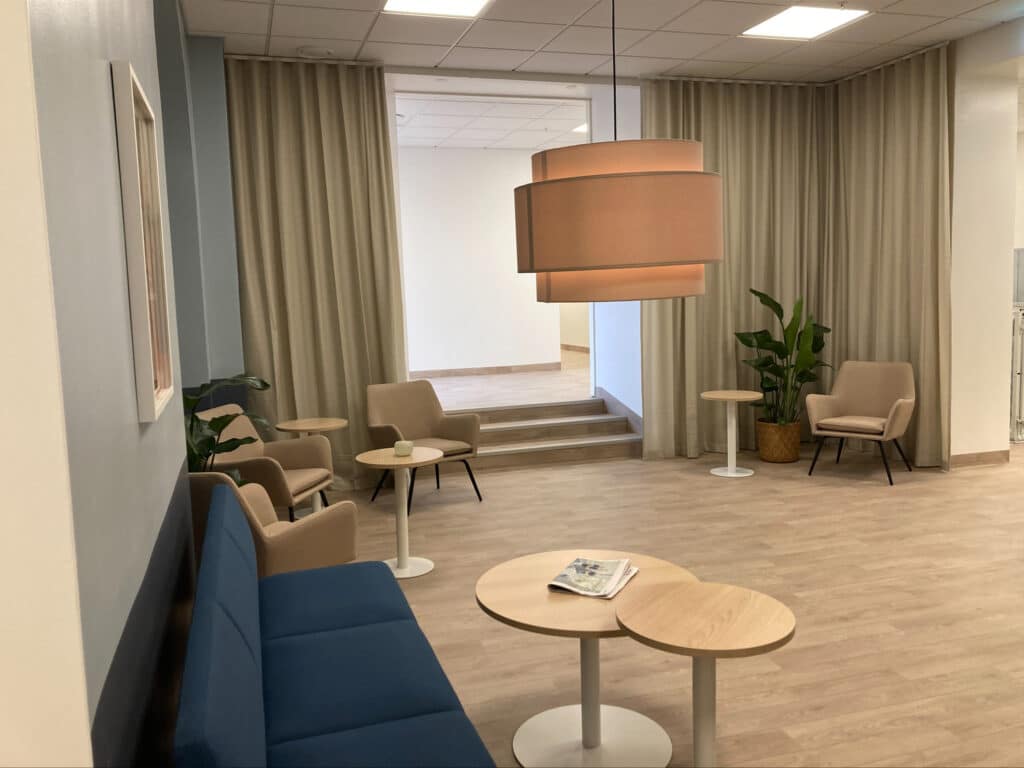 Väntrum på Smile Karlskrona med bekväma sittplatser, bord, och dekorativa lampor, inrett i en stilren och lugnande miljö med ljusa gardiner och moderna möbler.