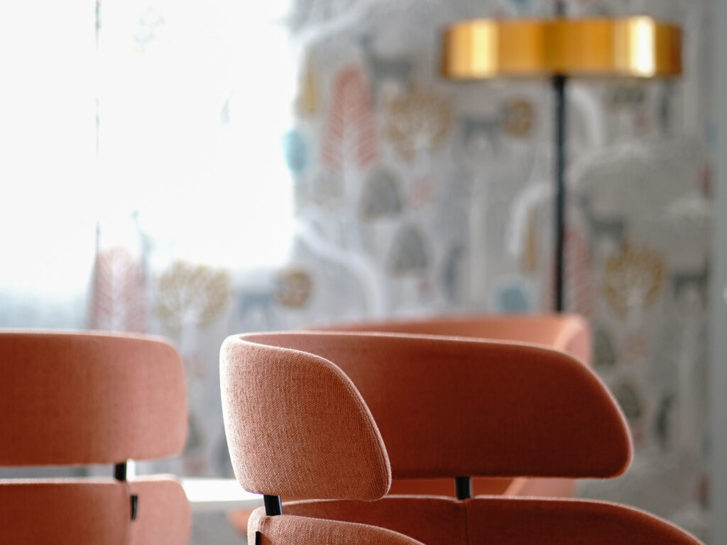 Närbild av orange stolar i ett väntrum, med mjukt dagsljus och en stilren inredning i bakgrunden, vilket skapar en varm och modern atmosfär