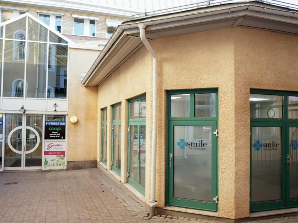 Exteriör av Smile Tandvård Kristinehamn med gröna fönsterramar och en gul fasad, belägen i en innergård.