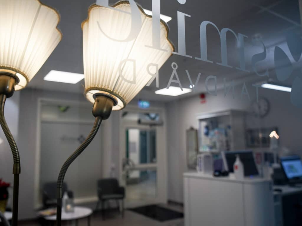 Receptionsområde på Smile Tandvård Kristinehamn med klassisk belysning, en modern reception och grå stolar i väntrummet.