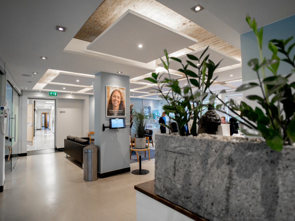 Väntrum på Smile Tandvård Malmö City med modern och stilren inredning. Svart skinnsoffa, träbord med växter och en ljus, inbjudande atmosfär.