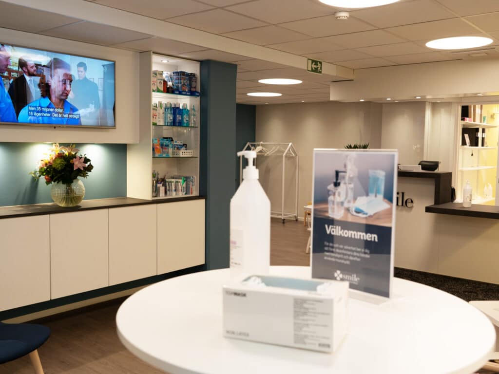 Receptionsområdet på tandklinik Smile Tandvård i Mölndal med välkomstskylt, sittplatser och en TV-skärm som visar information.