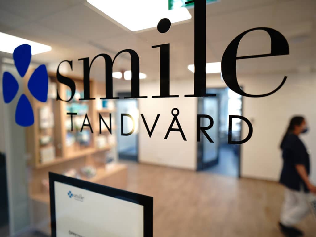 Närbild av Smile Tandvårds logotyp på ett glasfönster i klinikens interiör.