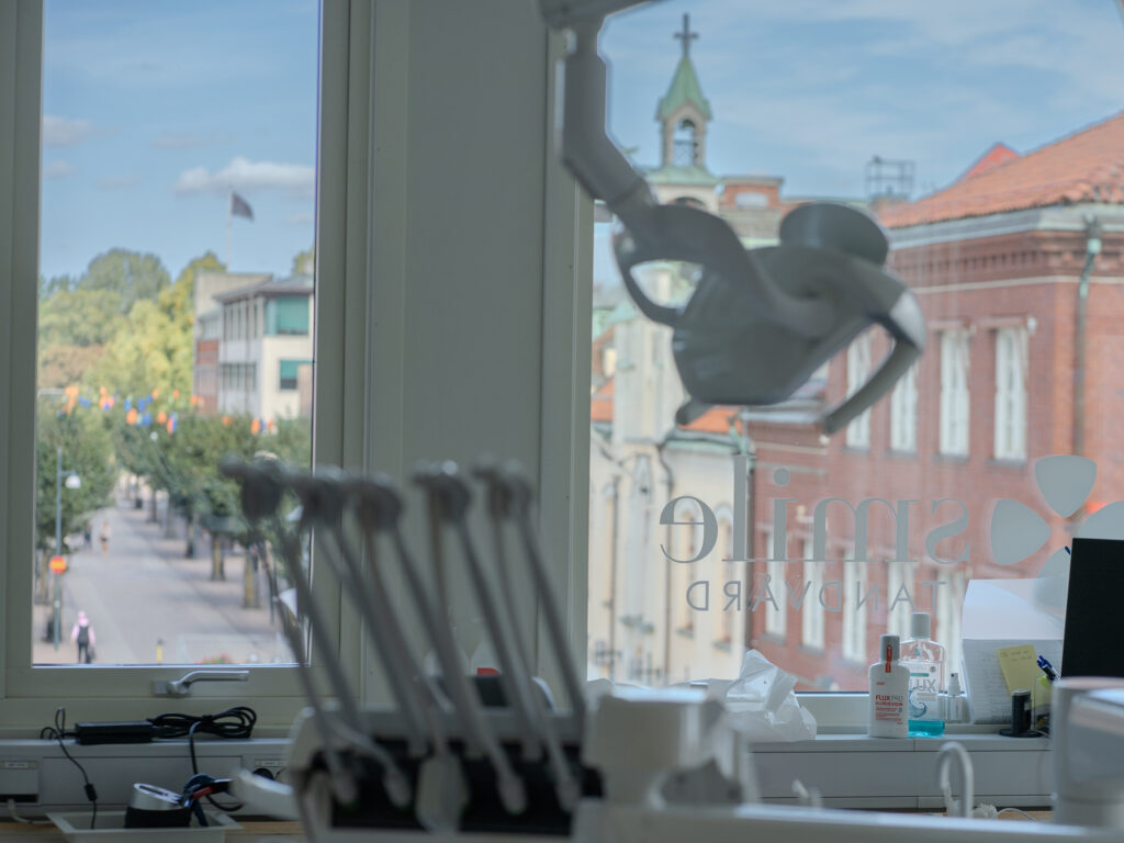 Utsikt från ett behandlingsrum på Smile Tandvård, med dental utrustning i förgrunden och stadsmiljö synlig genom fönstret.