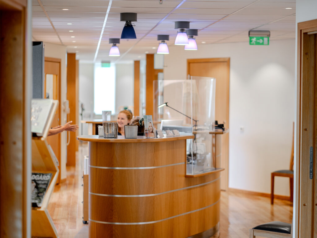Receptionen på Smile Tandvård med träinredning och en receptionist bakom disken, omgiven av ljusa och moderna korridorer.