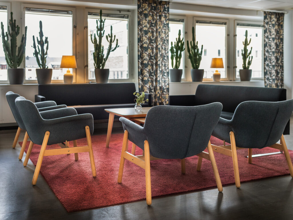 Modernt sällskapsrum med soffor, fåtöljer och små bord på röd matta.