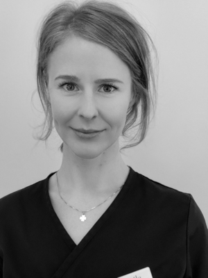 Svartvit bild av en team service medarbetare med ett lätt leende, uppsatt hår och iklädd en svart arbetsuniform, komplett med en namnbricka.