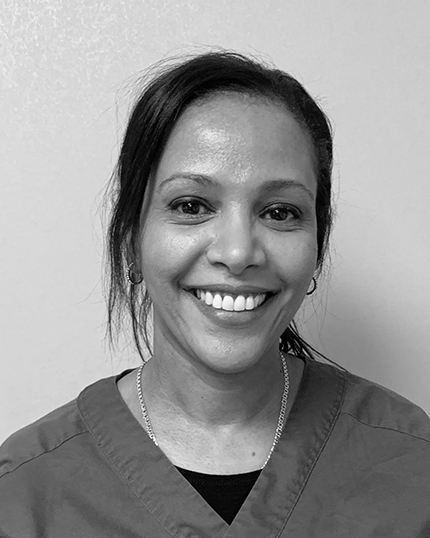 Svartvit bild av en leende kvinnlig tandhygienist om bär en mörk uniform. Hon verkar professionell och vänlig, vilket är egenskaper som är önskvärda hos någon som arbetar inom tandvård.