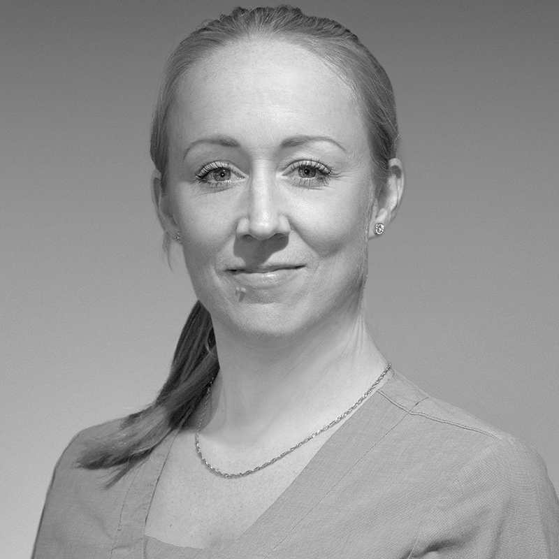Svartvit bild av en tandsköterska med uppsatt hår och ett självsäkert leende, iklädd en professionell uniform.