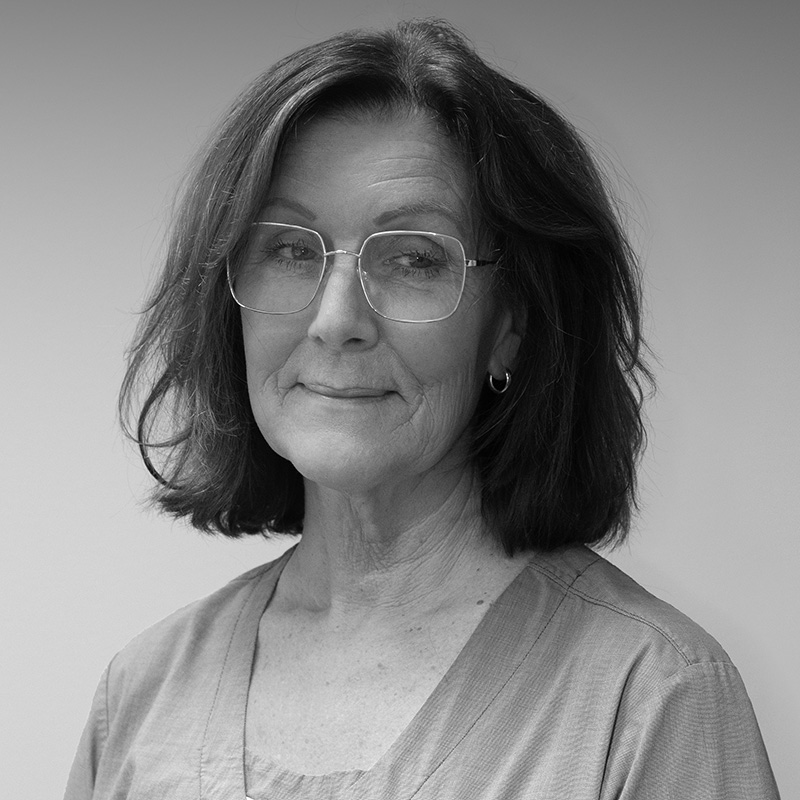 Svartvit bild av en tandsköterska med axellångt mörkt hår, glasögon, och ett halvleende, ser professionell ut i sin uniform.