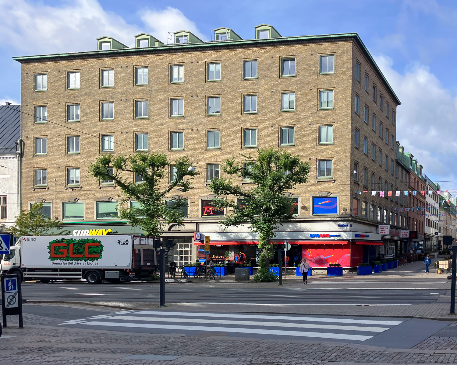 Gatuvy nära Göteborgs Domkyrka med synlig trafik, inklusive en lastbil och träd längs gatan och stadens typiska arkitektur i bakgrunden.