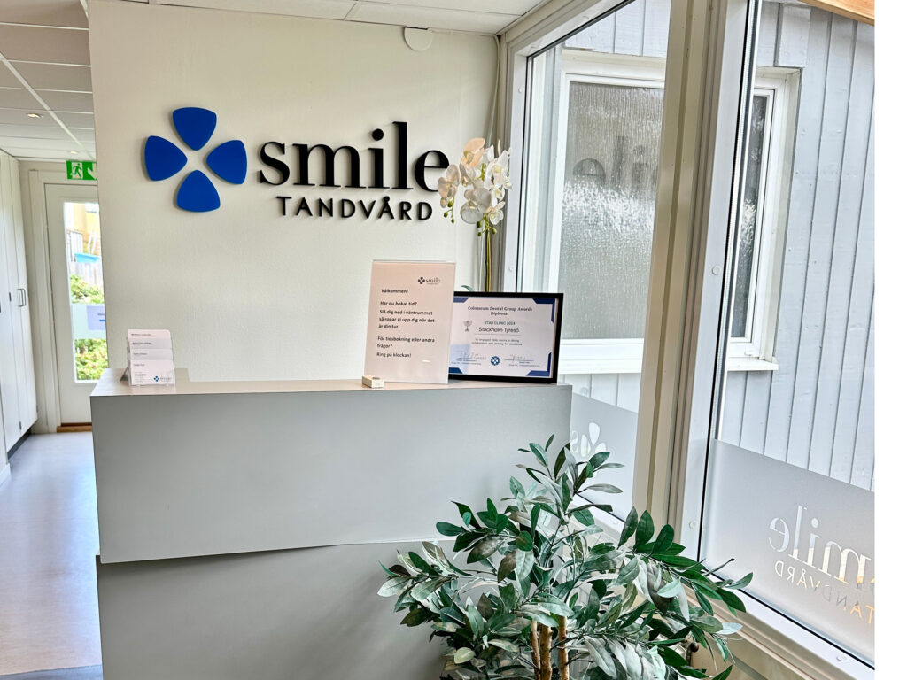 Receptionen hos Smile Tandvård med logotyp på väggen, informationsskylt och växtdekorationer.