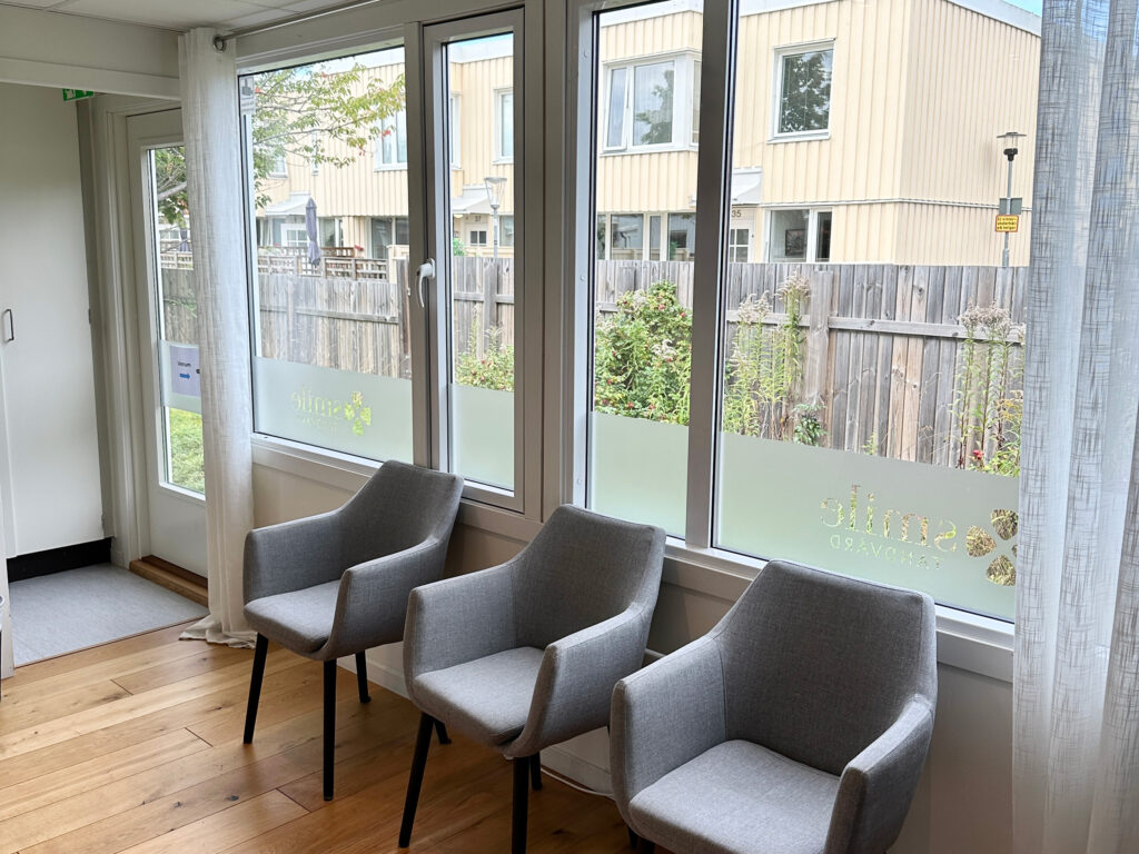 Väntrum hos Smile Tandvård med grå stolar och stora fönster som vetter mot en trädgård.