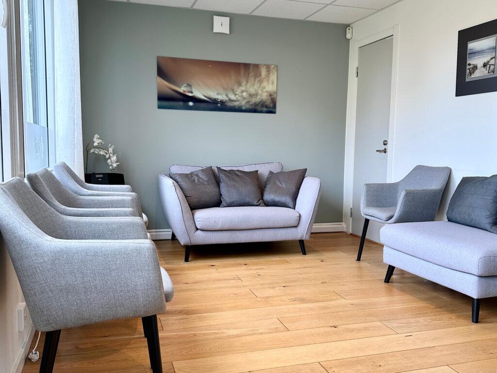 Väntrum hos Smile Tandvård Tyresö med grå soffor, stolar och ljus inredning.