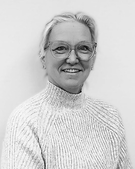Svartvitt porträtt av en leende person med kort ljust hår och glasögon med mörk båge. Personen bär en ljus tröja och tittar mot kameran mot en ljus, neutral bakgrund.