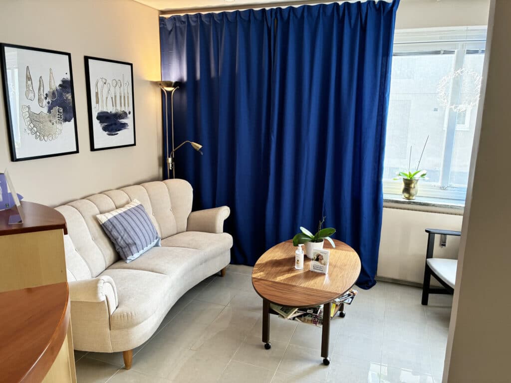 Ljust och modernt väntrum med soffa, bord och blå gardiner hos smile tandläkare i östersund.