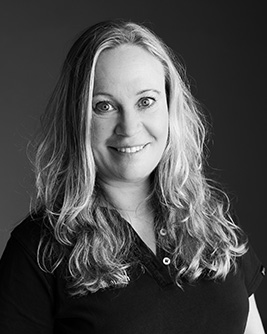 Porträtt av tandläkare, kvinna med långt hår, leende, svart arbetsklädsel.