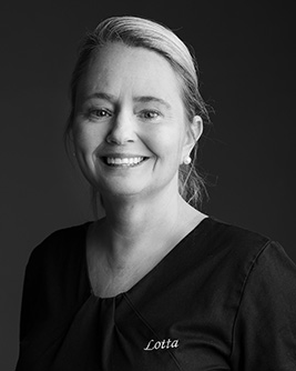 Porträtt av tandhygienist, kvinna med uppsatt hår, leende, svart arbetsklädsel.