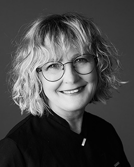 Porträtt av tandhygienist kvinna med kort hår och glasögon, leende, svart arbetsklädsel.