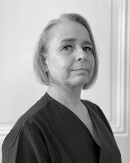 Svartvitt porträtt av en leende tandhygienist med ljust kort hår. Personen bär en mörk tröja och tittar mot kameran mot en ljus, neutral bakgrund.