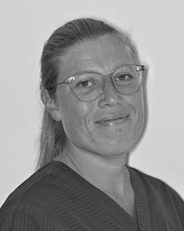 Svartvitt porträtt av en leende tandsköterska med uppsatt hår och glasögon mot en ljus bakgrund.