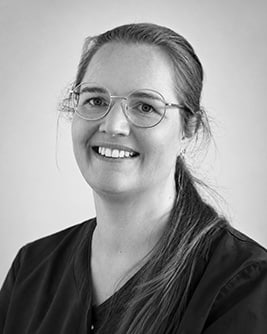 Svartvitt porträtt av en leende tandsköterska med uppsatt hår och glasögon mot en ljus bakgrund.