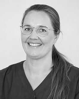 Svartvitt porträtt av en leende person med ljust mörkt hår och glasögon med ljus båge. Personen bär en mörk tröja och tittar mot kameran mot en ljus, neutral bakgrund.